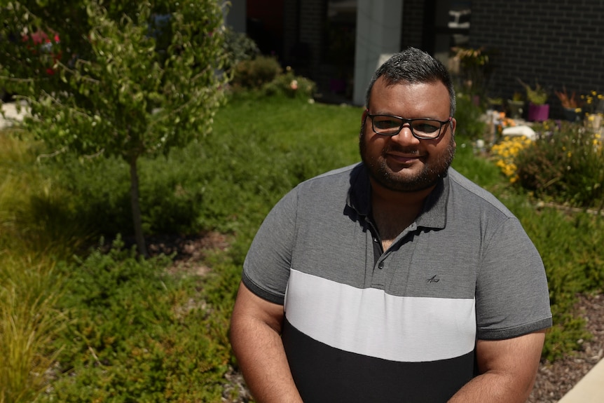 Rupain Saini smiling in his front yard surrounded by green garden.