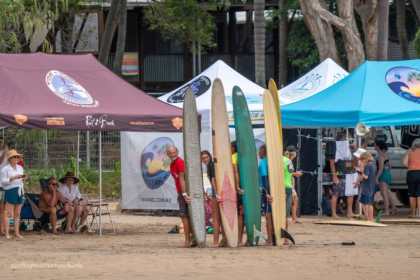 Men holding long boards standing on a beach