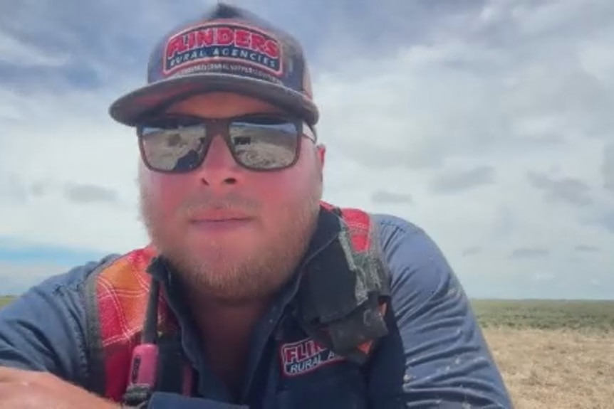 A man wearing sunnies and cap looking into camera. 