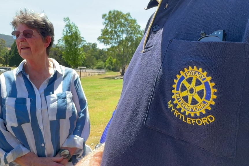 A close up of the Rotary logo on a shirt with a lady in the background.