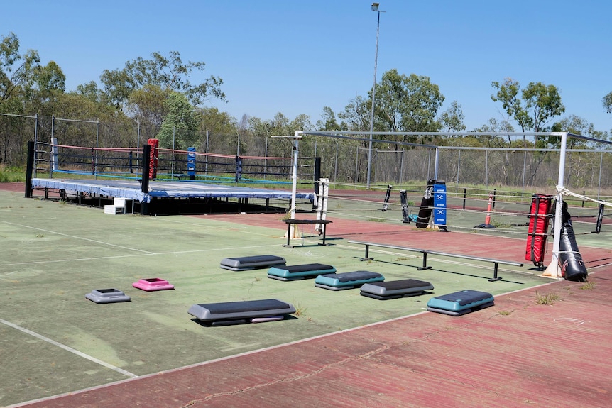 A concrete tennis court filled with gym equipment and a boxing ring.
