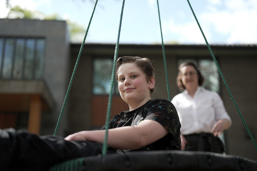A young white boy with short brown hair sitting in a tire swing