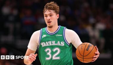 Cooper Flagg wearing a green Dallas Mavericks vest and holding a basketball in his left hand