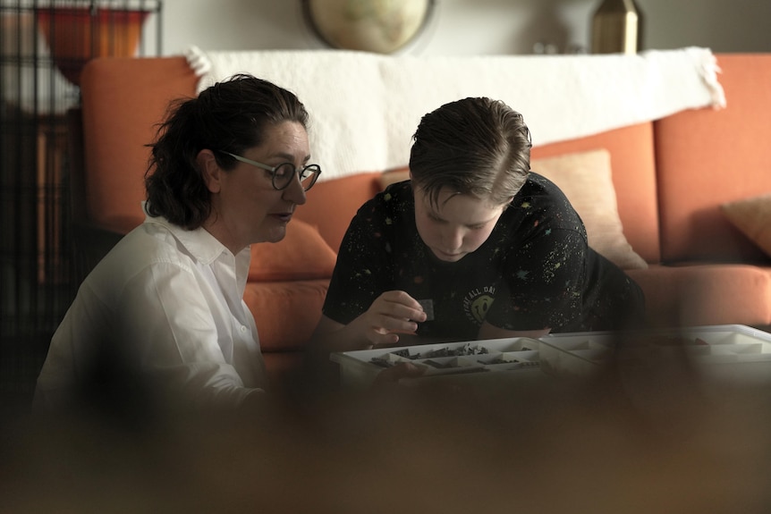 A young white boy with short brown hair with his mother, who has longer brown hair, playing with lego at a coffee table