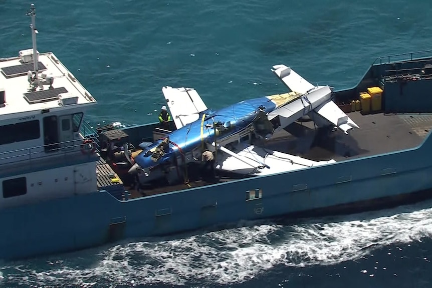 The wreckage of a small plane being pulled from the ocean by a barge. 