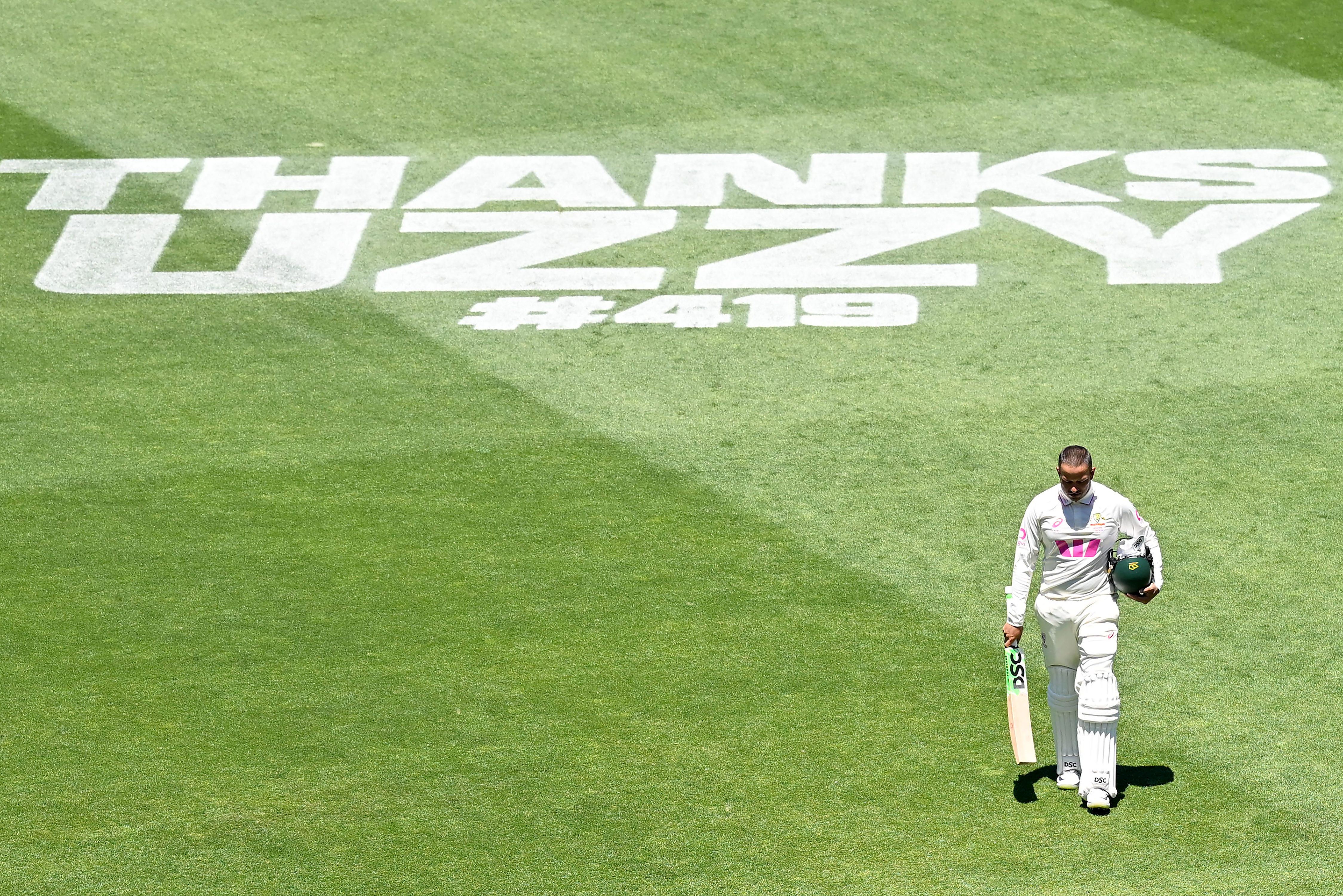 A cricket batter walks on grass with the words "THANKS UZZIE" written on it