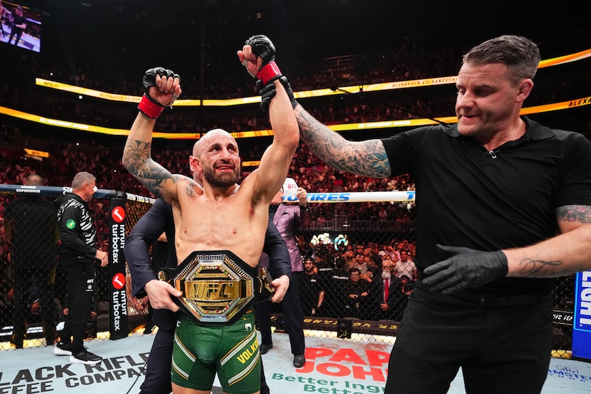 A man raises his arms in triumph after winning an MMA fight.