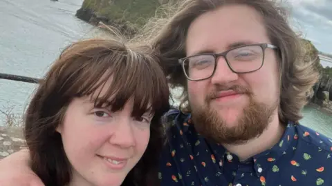 Lewis Relfe Ameila and Lewis Relfe smiling. Sea water can be seen behind them.