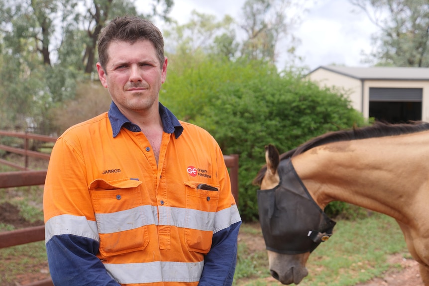 Jarrod Humphreys wearing an orange shirt while standing in front of a horse.