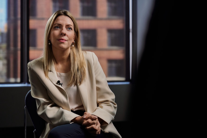A woman dressed in business attire sits in an office looking towards someone elevated in the foreground.