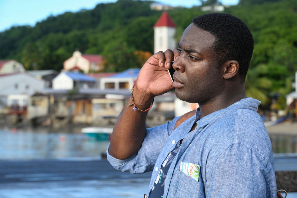 person holding their hand to their ear surrounded by a coastal landscape