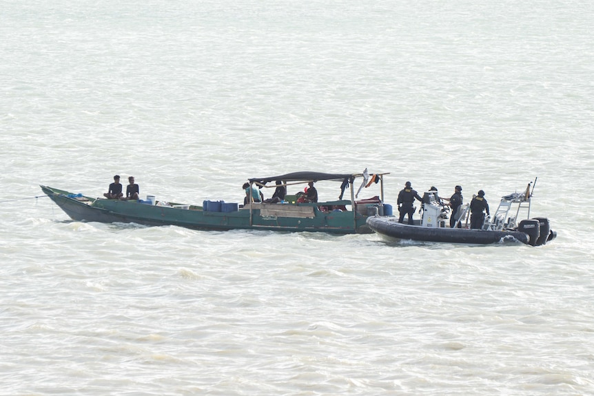 People being moved off a wooden boat onto an inflatable boat.