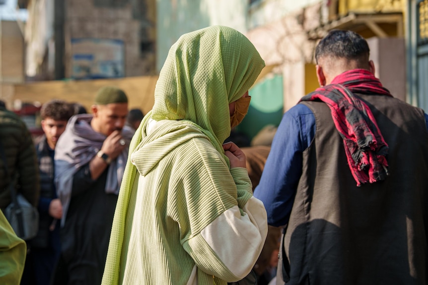 A woman wearing a bright green hijab walks along a street in Kabul