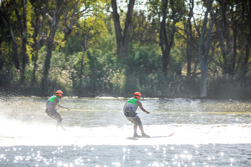 Two water skiers hold on to a rope while skiing on sun-kissed river water