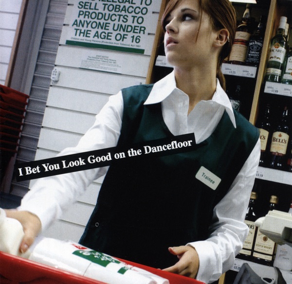 A young female corner store clerk, wearing "trainee" badge glances out shopfront. Text reads: I Bet You Look Good On the Dancefl