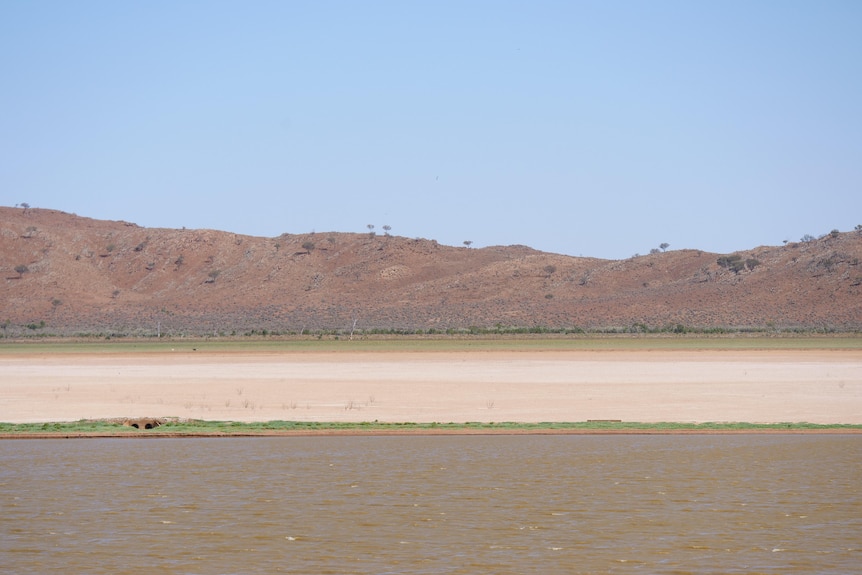 An expanse of water shows in the foreground, with a stretch of dry lakebed and mountains under a clear sky in the background