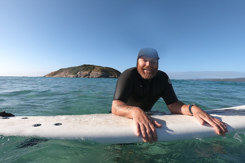 Riley Coffey rest his arms on a surfboard. 