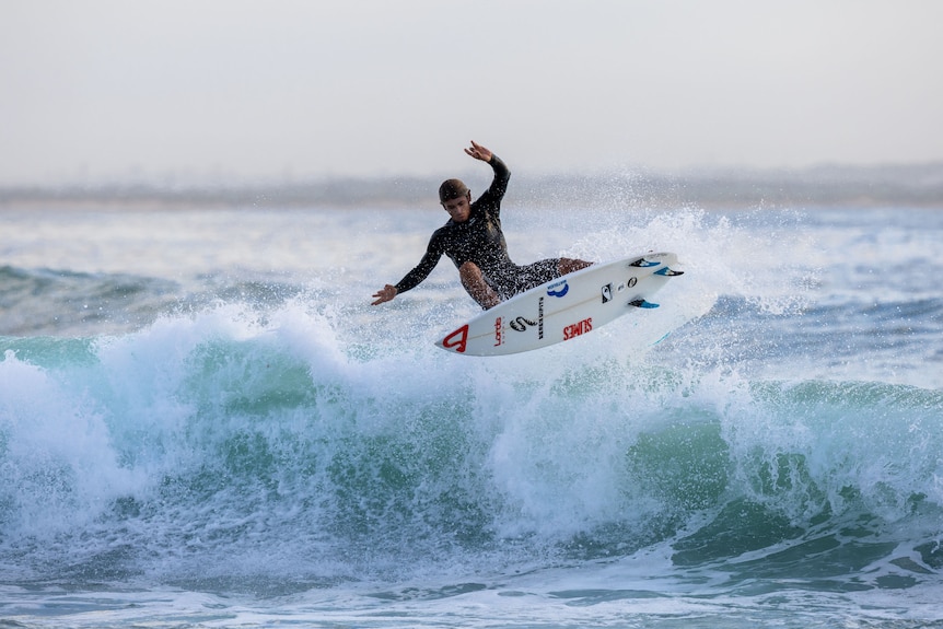 A man on a surf board in the air above a wave.