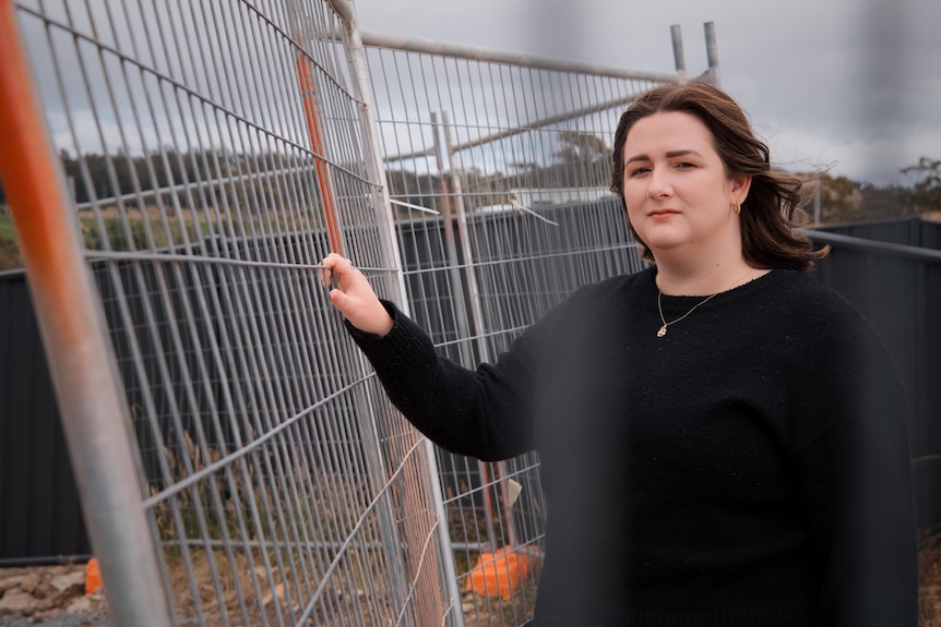 Erin Bell stands with her hand against a mesh fence
