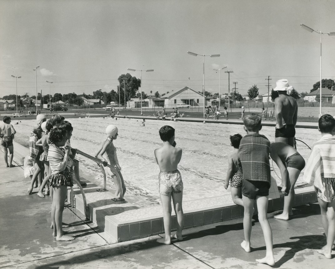 A black and white photo of children standing around an Australian suburb public pool in the 1960s