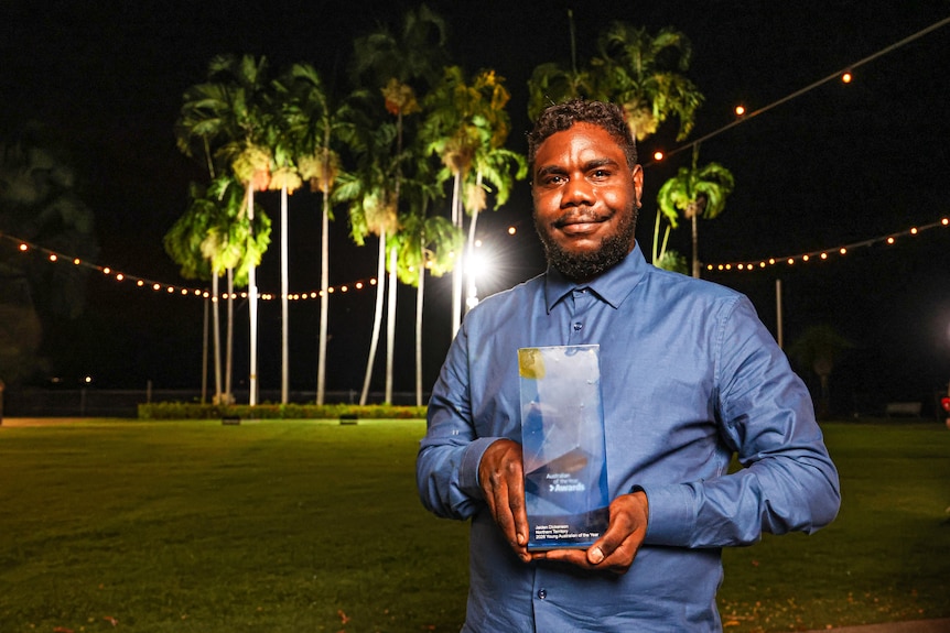 A man holding an award smiles at the camera. 