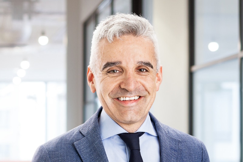 A 50-something man with white hair and a grey suit smiles at the camera.
