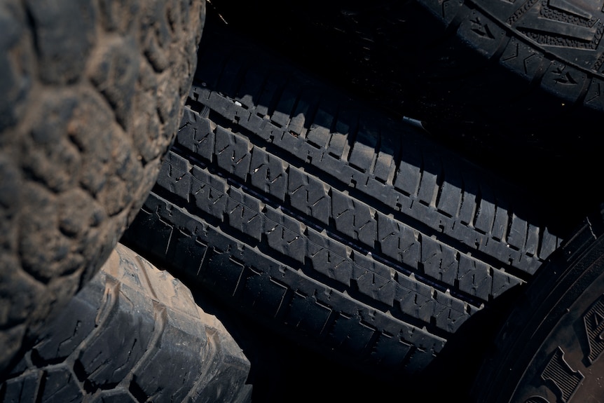 A close-up of an old tyre, sitting in a pile of other discarded tyres.