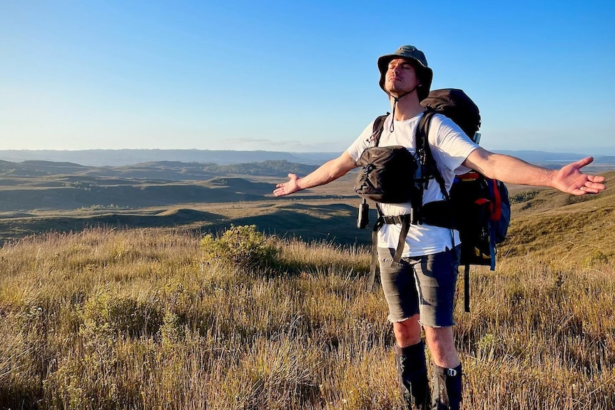 A bushwalker stands in button grass with eyes closed and smiles in the sun