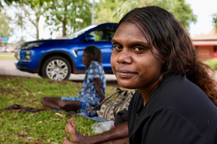 Aboriginal young woman with long hair sitting on the grass with older women