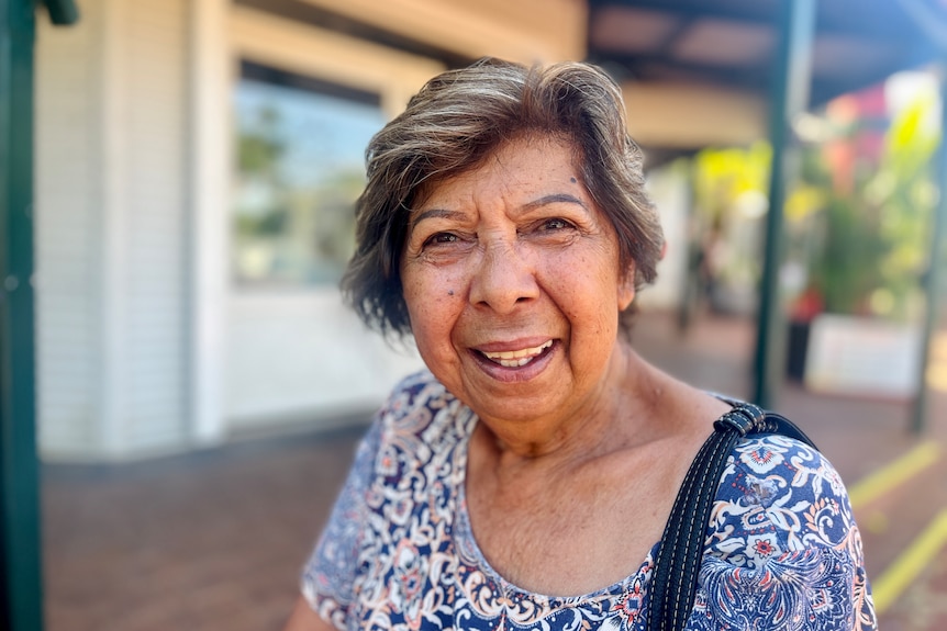 A woman wearing a patterned outfit smiles. She has short brown hair.