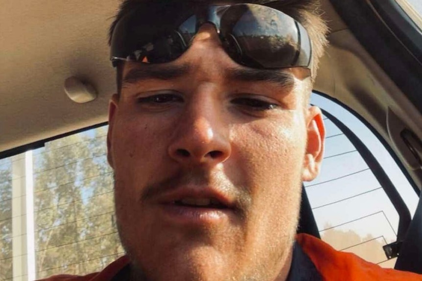 Portrait of a young man with spiky blonde hair and sunglasses resting on his on forehead.