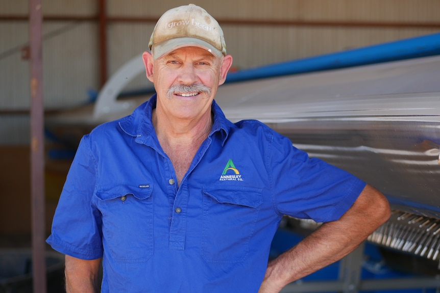 A man in a blue shirt with a moustache smiling at the camera