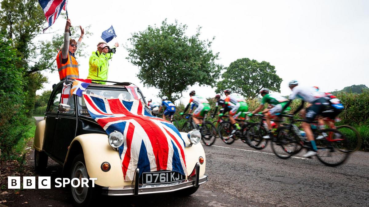 Fans wave flags in a car draped in a union jack as riders go past