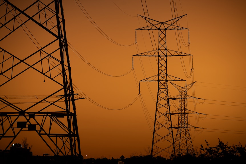 Powerlines suspended between towers against orange dusk sky.
