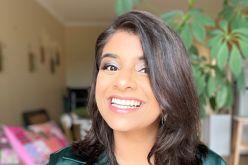 A headshot of a smiling young woman of South Asian appearance with long brown hair.