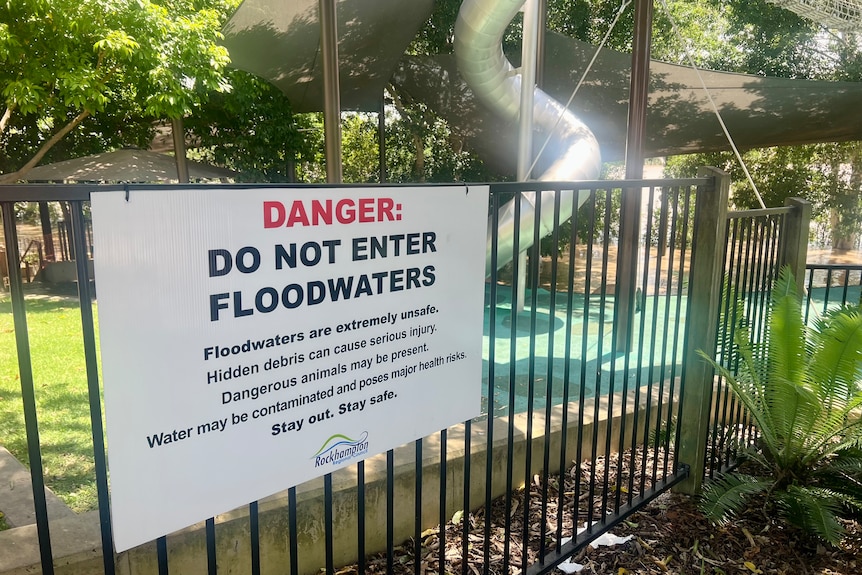 A sign tied to a playground fence telling people not to enter floodwaters 