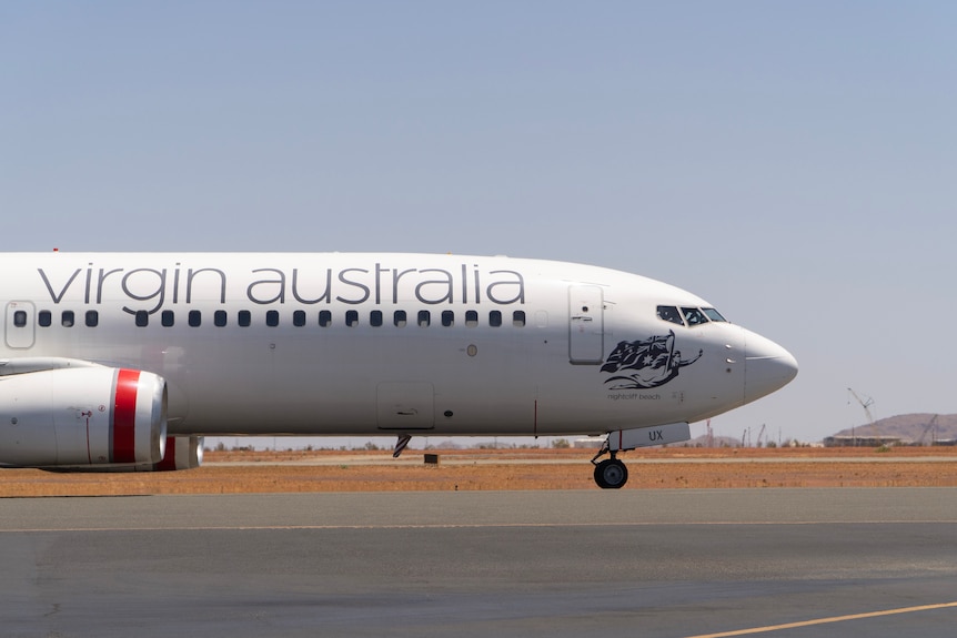 A plane with the branding 'Virgin Australia' on a tarmac set in front of red dust.