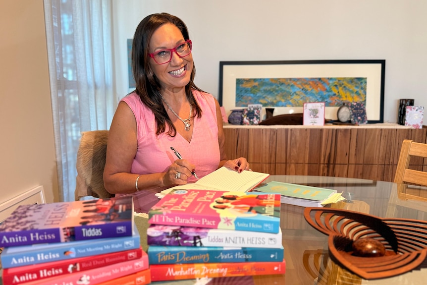 A photo of Dr Anita Heiss smiling signing her books.