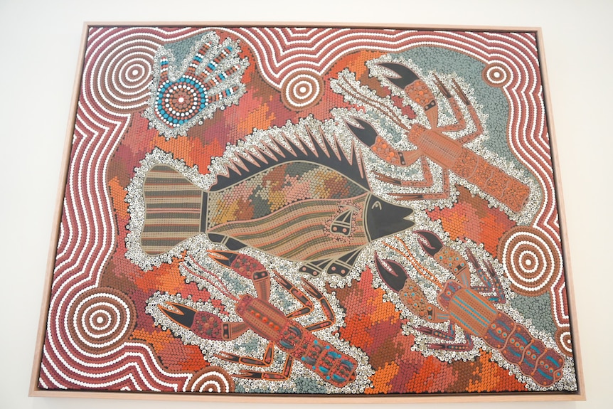 An Aboriginal artwork painted with white and ochre colours featuring a large fish in the middle surrounded by crustaceans. 