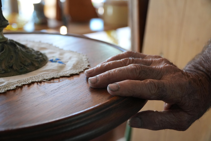 A close-up shot of an older man's hand resting on an antique table.