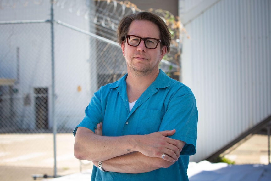 A man in glasses and a blue button up shirt with his arms crossed.