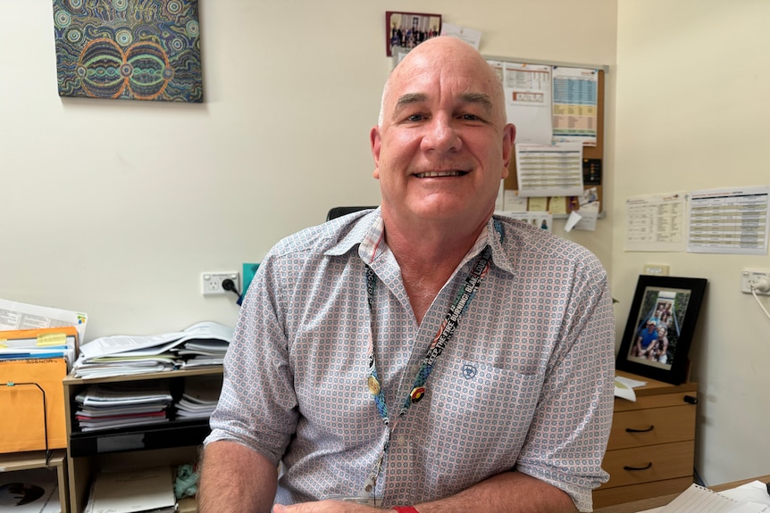 A man in a collared shirt smiles at the camera in an office setting