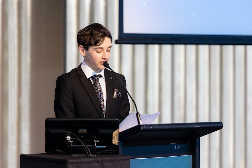 A young man in a suit giving a speech at a lecturn