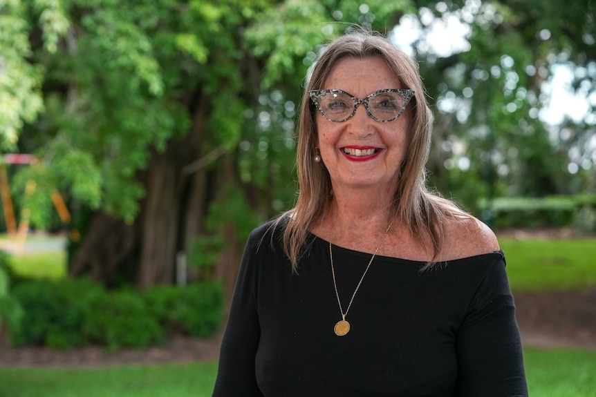 A woman with shoulder length hair and glasses smiles at the camera.