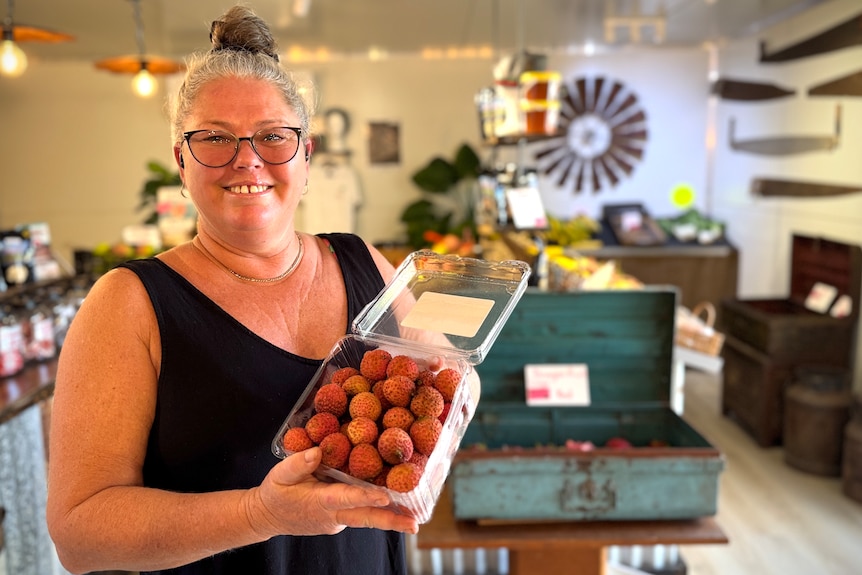 A woman holding up lychees, smiling at the camera.