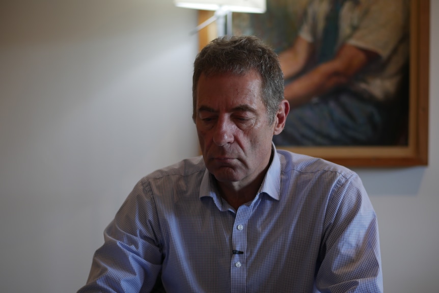 Man seated at table looking down at something, with a light in the background casting a halo