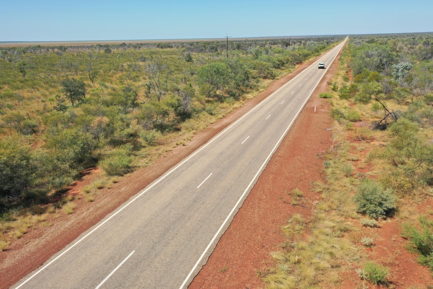 A ute drives along a lonely highway in the outback