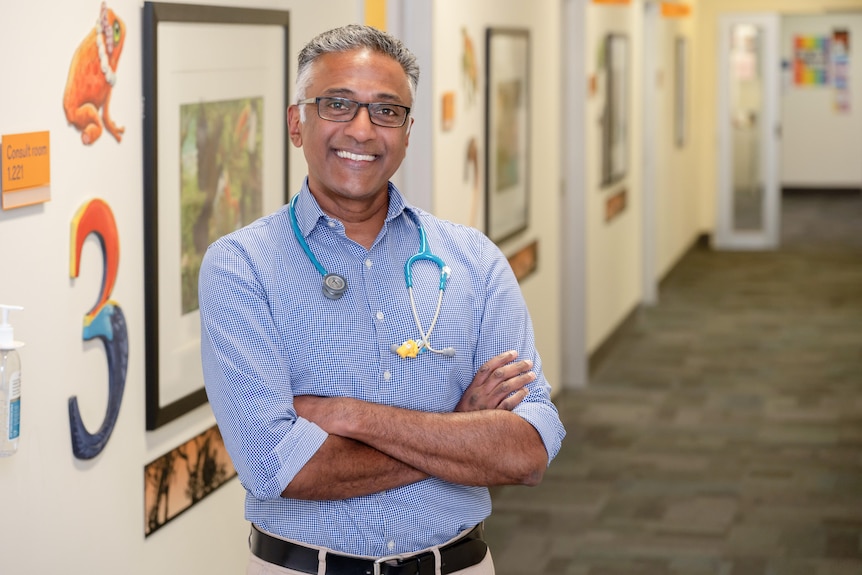 A middle aged man of South Asian background wearing a blue shirt with a stethoscope around his neck