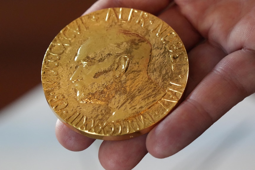 A handing holding a gold replica of the Nobel Peace Medal