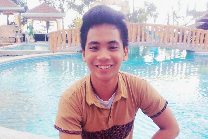 A young man sitting on the edge of a pool and smiling.